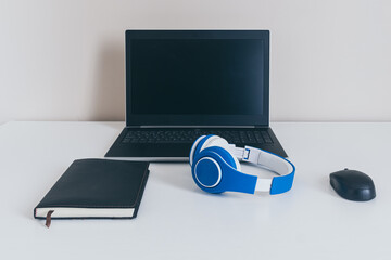 laptop with mouse and blue headphones on white table