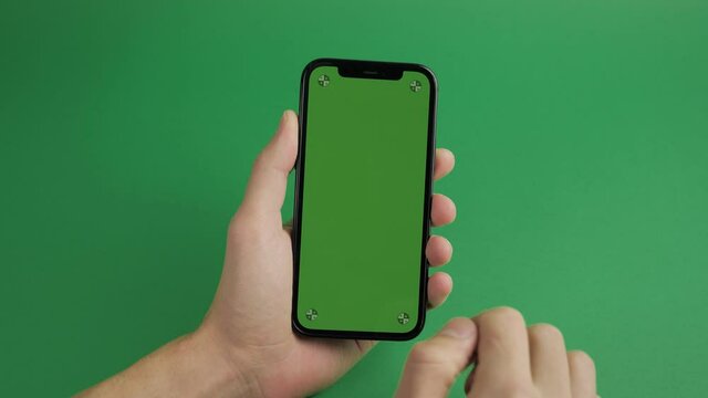 Close-up of male hand holding mobile telephone with vertical green screen chroma key smartphone technology cell phone touch message display hand on green background.