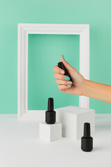 Womans hand holding bottle of nail varnish over turquoise background