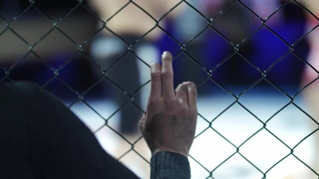 The trainer of the fighter holds on to the metallic mesh during the fight in mixed martial arts. Fighters hit each other
