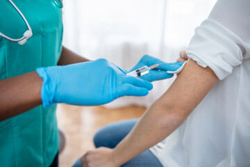 Hands of doctor in medical gloves injecting vaccine to a patient. Doctor giving muscular injection to woman. Vaccination healthcare concept. Selective focus on syringe and vial.