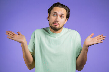 Young indifferent unsure man makes gesture of I dont know, cant help anything. Difficult question concept. Violet studio background.
