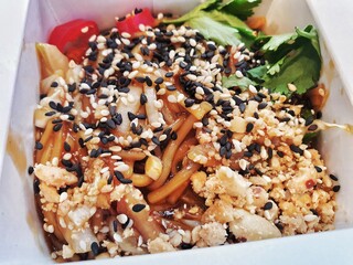 Wok noodles with vegetables topped with sesame and served in the box to take away. Close-up view.