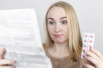 Girl on a white background reads the instructions for medicines. The woman looks at the list and...