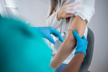 Vaccination, immunization, disease prevention concept. Woman in medical face mask getting Covid-19 or flu vaccine at the hospital. Professional nurse or doctor giving antiviral injection to patient