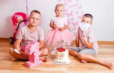 Obraz na płótnie Canvas three children sit on the floor on the girl's birthday. beautiful pink design and prassy white cake with strawberries