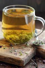 Thyme herbal tea in a glass cup with dry herb on rustic wooden board, healthy aromatic drink is for blood pressure, cough remedy, immune support, closeup, naturopathy medicine concept