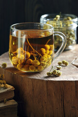 Tansy seed tea or infusion in a glass cup with flowers on wood with books nearby, herbal drink is good as anthelmintic, menstrual, kidney, rheumatism remedy , closeup, naturopathy, homeopathy concept