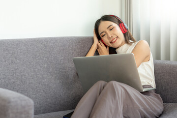 A young Asian woman is happily relaxing listening to music through wireless headphones while at home on vacation.