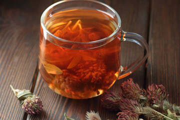 Red clover tea in glass cup on wood on rustic background of wicker, herbal drink is good for menopause, bone, heart health and for skin and hair care, closeup, naturopathy and natural medicine concept