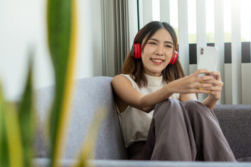 A young Asian woman wears headphones wirelessly, connects to a bluetooth system with a mobile...