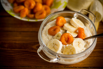cooked boiled sweet oatmeal with with dried apricots and bananas in a bowl