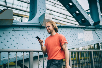 Smiling hipster walking on bridge with cellphone