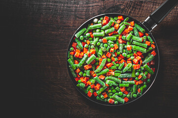 Mixed vegetables. green beans, peas and carrots in an iron pan on a wooden background