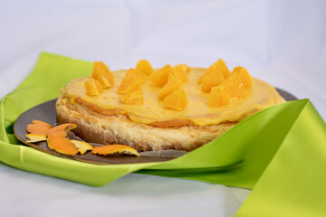 Tasty homemade vanilla cheesecake on the wooden desk with fresh sliced orange on top decorated with peels of orange and green ribbon.