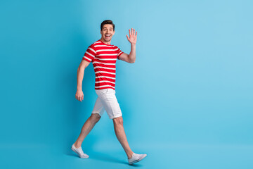Full length body size side profile photo man walking waving hand meeting isolated on bright blue color background © deagreez
