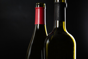 two open bottles of wine stand side by side on a dark glossy background.