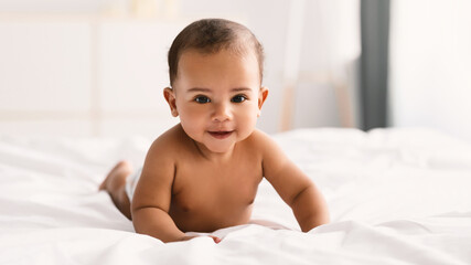 Cute little African American infant lying on bed