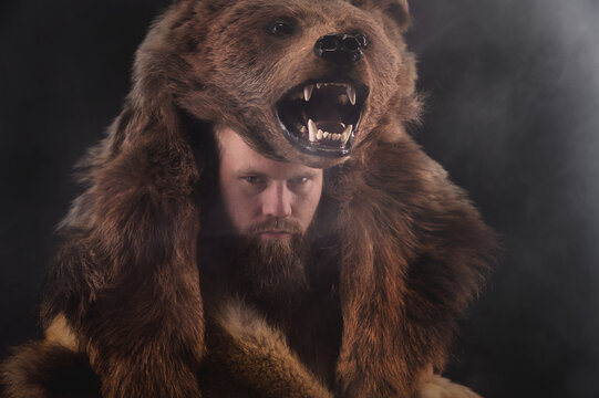 Low key portrait of a bearded war shaman in bearskin with an ancient ax in his hands. High quality cosplay of the ancient werewolf war