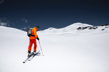 Fototapeta na wymiar Portrait of a young male athlete skier in a ski tour on skis on the background of snow-capped mountains on a sunny day. Skitour professional