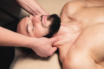 Fototapeta na wymiar Professional neck massage to a bearded male athlete in a dark room of a spa massage room