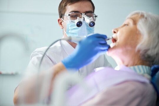 Dentist In Dental Headlights Loupes Treating Old Woman Teeth