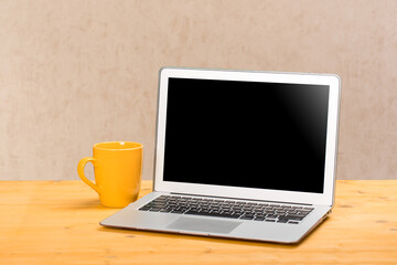 Fototapeta premium Laptop with blank screen for product display and cup of coffee on wooden table