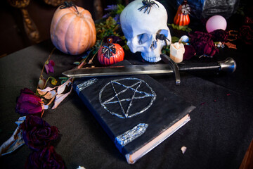 Focus on a black book with a pentagram lying on a black table against a background of a skull and...