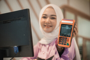 portrait of asian attractive cashier muslim showing edc machine to camera