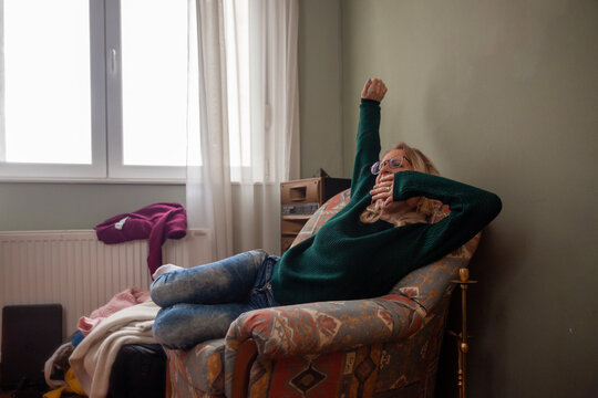 One Young Woman, Yawning And Stretching At Home, Sitting In Sofa.