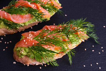 two delicious crispy canapes with avocado and smoked salmon fillet and fresh dill sprigs and...