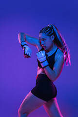 Athletic female MMA fighter training over blue-pink background in neon light