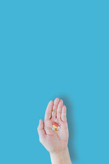 Various colorful medical pills in hand on blue background, vertical orientation