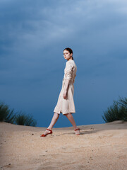 Woman in a sundress in red shoes gesturing with her feet on the sand on the beach