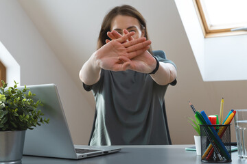 Working from home exercise. Young woman stretching hands while sitting at desk. Healthy living...