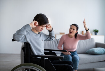 Obraz premium Teenage boy in wheelchair having fight with his angry mom, closing ears not to hear her quarreling at home