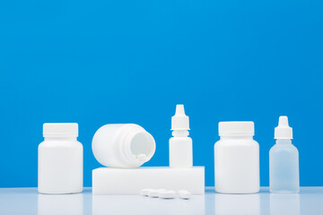 White plastic bottles with different medications, pills, nose spray and eye drops on white table against blue background with copy space. 