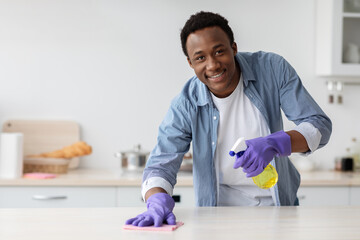 Smiling african american guy cleaning kitchen furniture, copy space