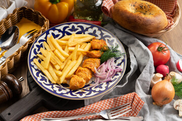A portion of chicken shish kebab with French fries, onions and dill