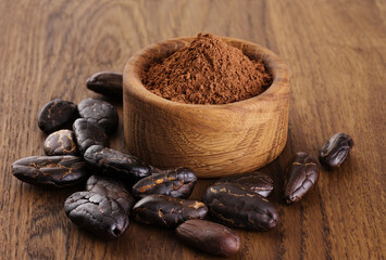 Cocoa beans and powder in bowl on wooden background.