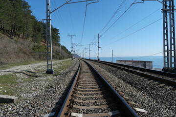 Railroad rails with concrete sleepers and electric wires. There are mountain and sea around....