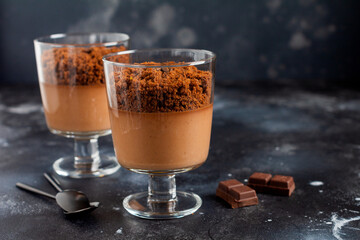 Chocolate mousse with brownie in glass jars on a dark slate, stone or concrete background. Delicious dessert. Selective focus