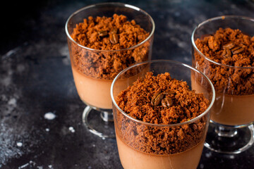 Chocolate mousse with brownie in glass jars on a dark slate, stone or concrete background. Delicious dessert. Selective focus