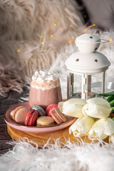 Obraz na płótnie Canvas A glass of hot cocoa with marshmallows, macaroni cakes and white tulips on a tray in bed. Cozy spring home concept, vertical photo