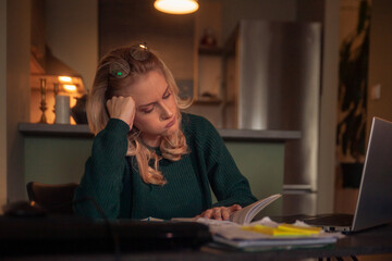 one young woman, reading from a book, late at night at her tome, sitting on a desk.