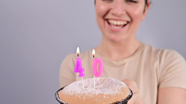 The happy woman makes a wish and blows out the candles on the 40th birthday cake. Girl celebrating birthday.