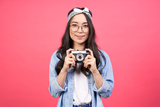 Beautiful cheerful young asian woman holding retro style camera on pink background.