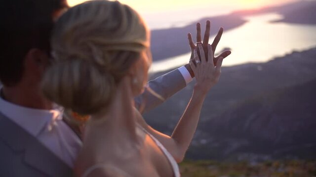 The bride and groom are embracing and watching sunset over the Bay of Kotor, the bride put her hand on the groom's hand 