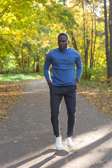 Cheerful african american young man in stylish clothes walks in autumn park on sunny warm autumn day. Concept of weekend and outdoor recreation