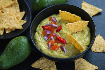 Close-up of guacamole dipping sauce in a black bowl with nachos chips, selective focus, studio shot